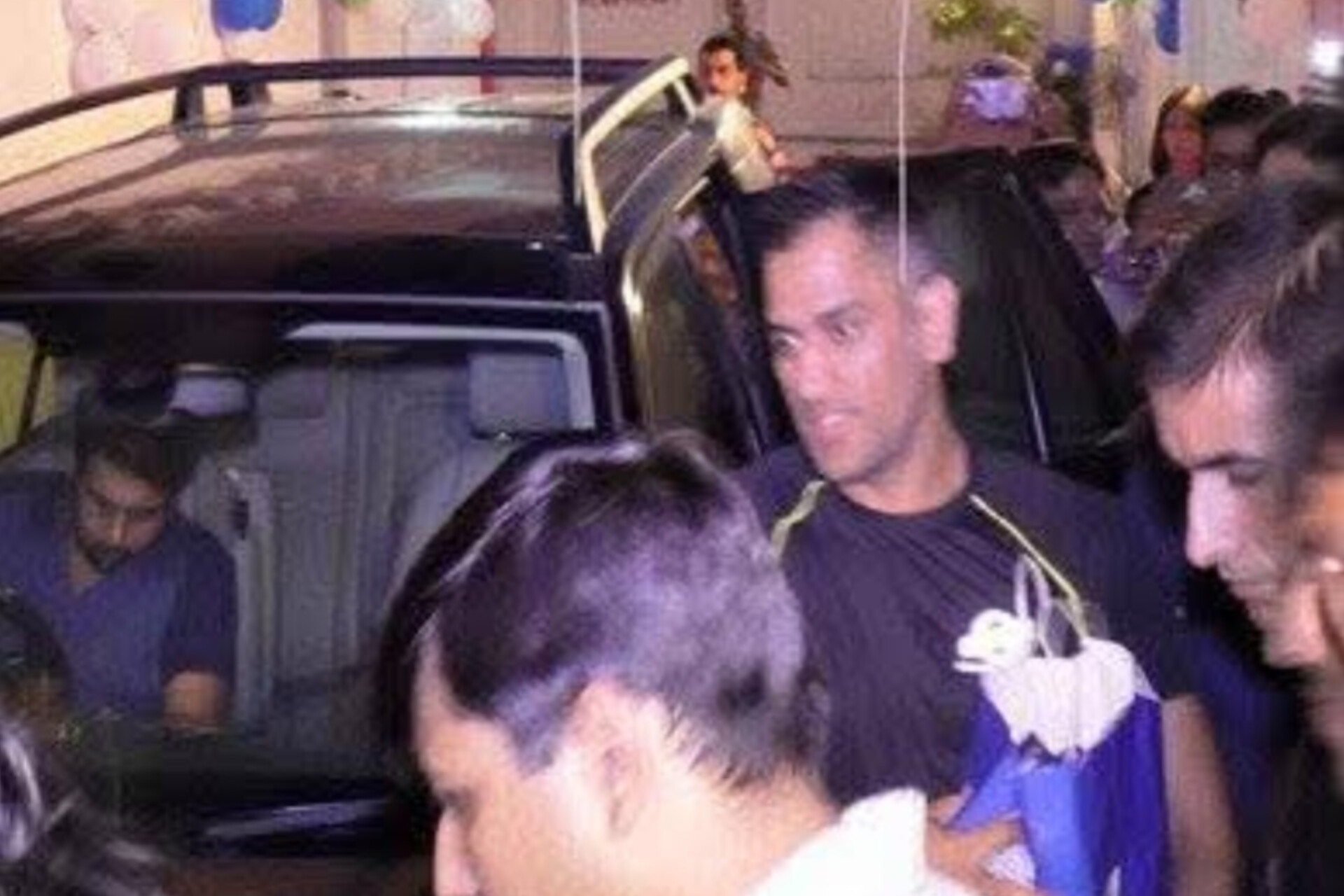 Archival photograph from MS Dhoni’s July 2016 Varanasi gym visit, showing a man in sportswear moving through a crowd beside a vehicle in Mahmoorganj.