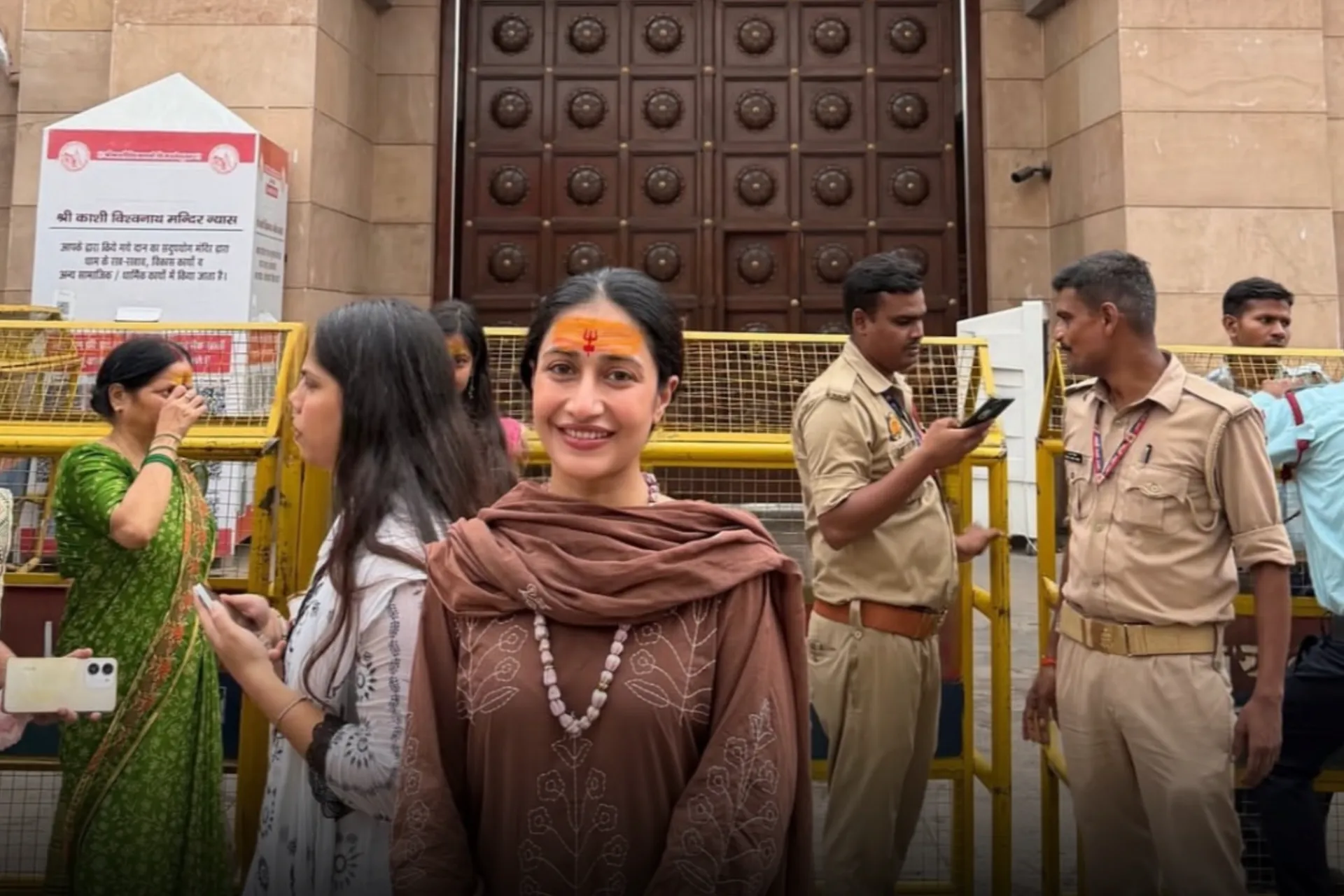 Dhanashree Verma wearing a brown ethnic outfit and saffron tilak outside Shri Kashi Vishwanath Temple during her Varanasi visit.