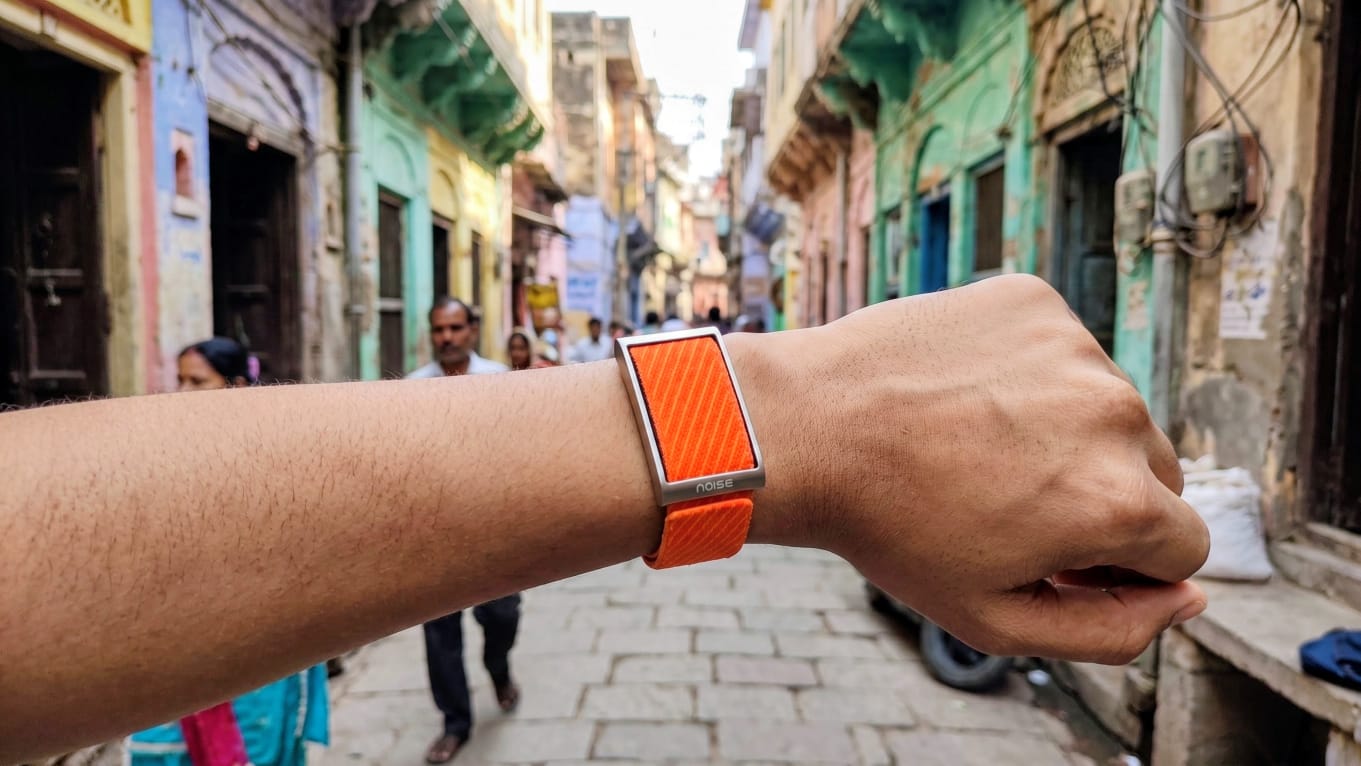 Vivid Orange Noise REP Band worn on a wrist in a narrow Varanasi street.