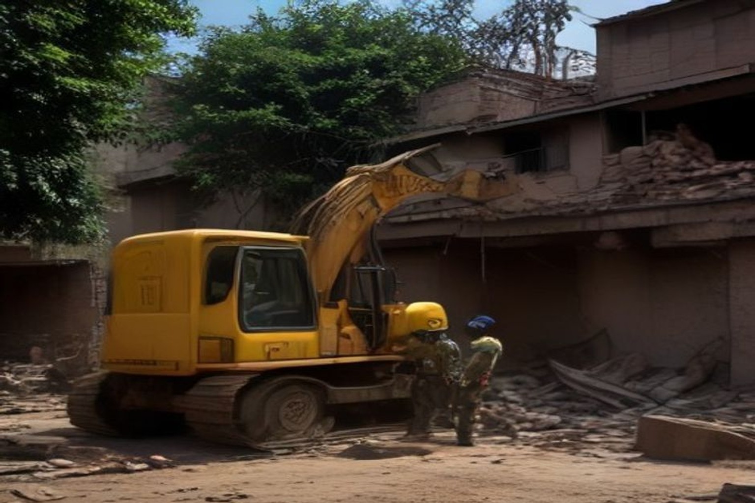 A yellow tracked excavator works beside a partially demolished two-storey brick house as two uniformed officers stand in the dust watching the demolition.